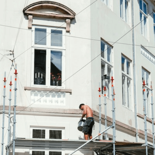 Mann steht auf Gerüst an der Fassade eines Gebäudes mit Eimer in der Hand